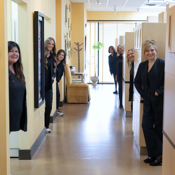 Multiple staff members standing along a clinic hallway between treatment rooms and office work areas.