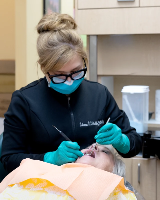 Johnna Shockley wearing protective equipment performing an oral examination on a reclining patient.
