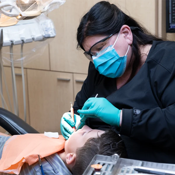 Dental professional wearing protective equipment performing an oral procedure on a reclining child patient.