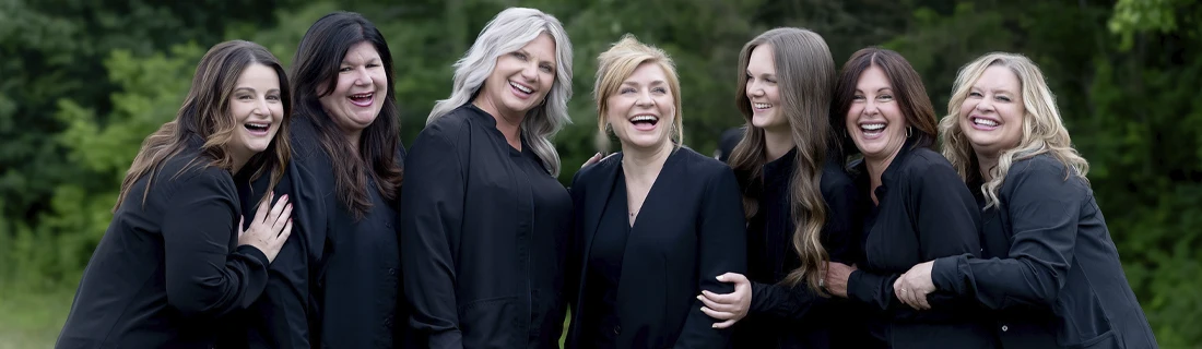 Group portrait of six staff members standing outdoors wearing matching dark-colored attire.