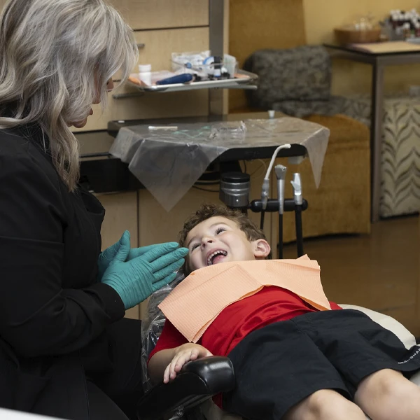 Dental professional wearing gloves interacting with a child reclining in a dental chair.